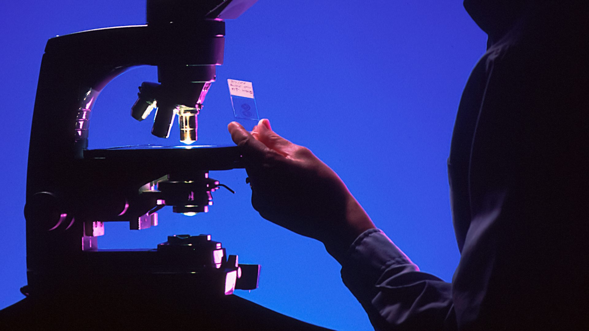A researcher at a microscope in a dark laboratory