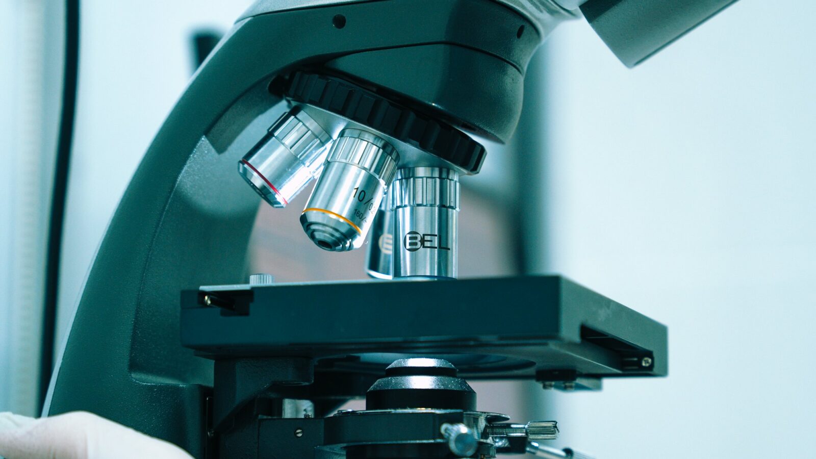 A gloved hand adjusting a laboratory microscope