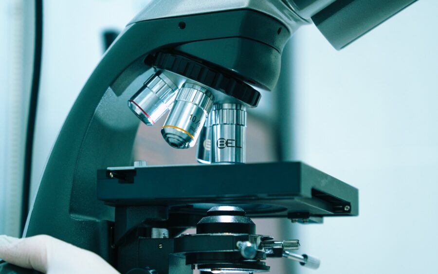 A gloved hand adjusting a laboratory microscope
